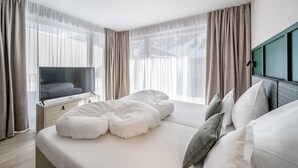 Una habitación de hotel moderna con una cama grande, un televisor de pantalla plana y vistas al exterior a través de cortinas translúcidas.