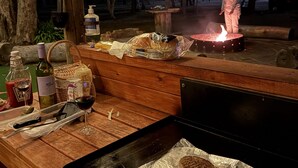 Área de churrasco externa com churrasqueira, alimentos e uma garrafa de vinho.