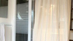 Un baño con cortina de ducha blanca, una toalla blanca y un tapete de baño blanco en el suelo.