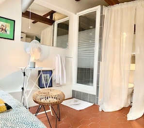 Un baño con cortina de ducha, un perchero, un ventilador y un taburete pequeño.