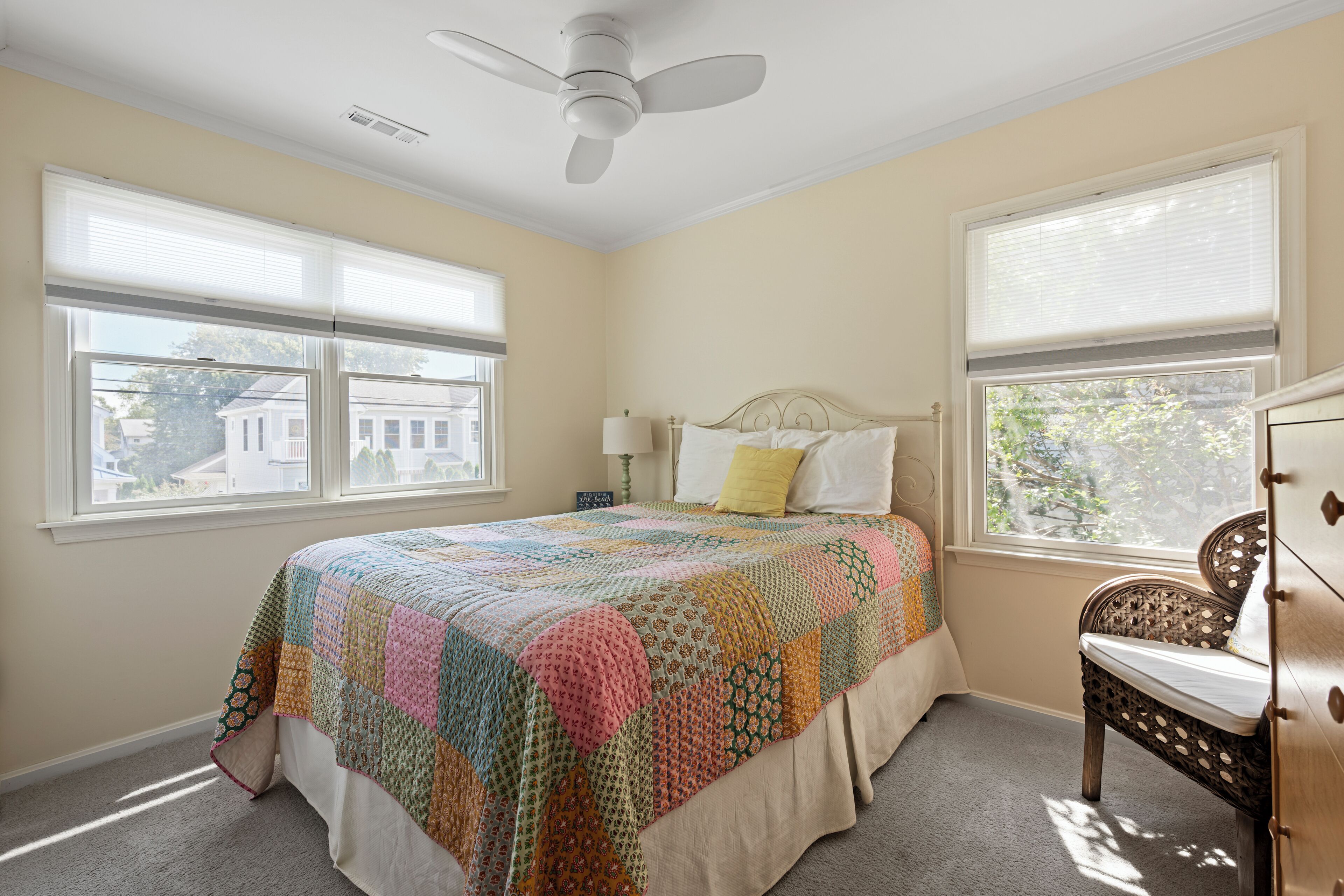 A bedroom with a large bed, two windows, a ceiling fan, and a dresser.