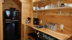 A compact kitchen with wooden walls, a black refrigerator, and built-in shelves with dishes and utensils. - Maple Ridge Creek in the North Georgia Mountains (Morganton)