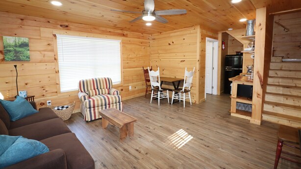 A wooden cabin interior with a sofa, striped armchair, dining table, and chairs. - Maple Ridge Creek in the North Georgia Mountains (Morganton)