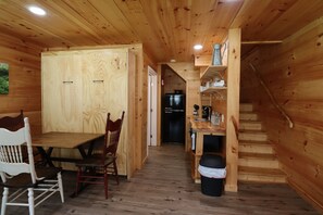 A wooden cabin interior with a dining area, kitchen, and staircase.