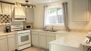 Une cuisine avec des meubles blancs, une cuisinière, un four à micro-ondes, un évier et une fenêtre avec des rideaux.