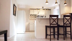 Une cuisine avec des meubles blancs, un réfrigérateur blanc et un coin bar équipé de deux chaises en bois.