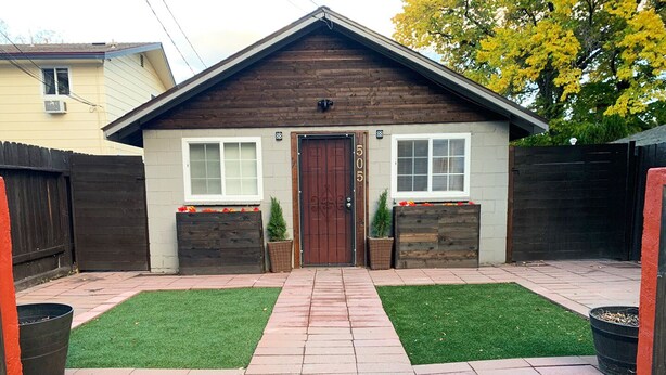 Une maison avec une porte marron, deux fenêtres et le numéro « 50 » sur la porte.