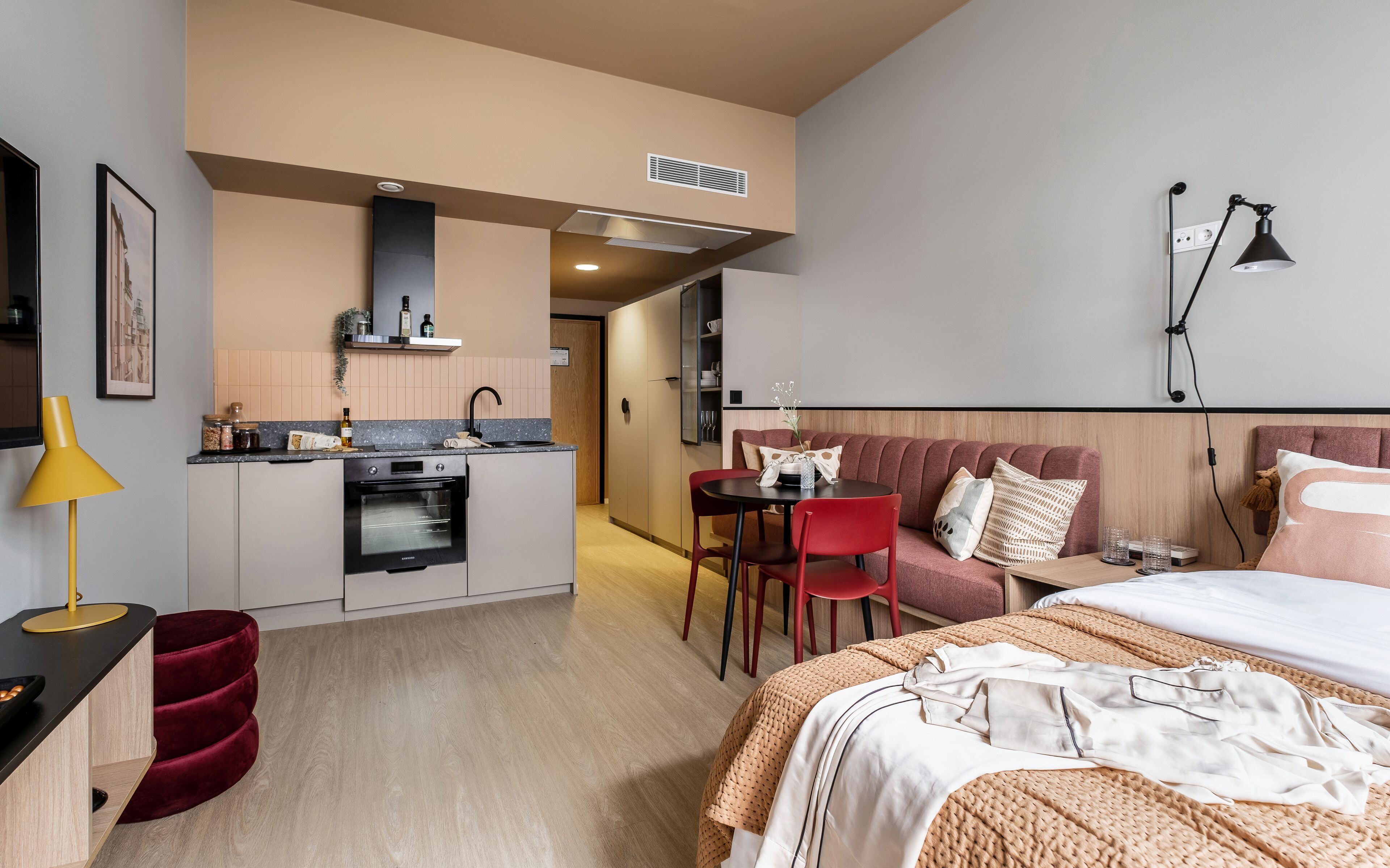 A modern hotel room with a kitchenette, a dining area, and a bed.