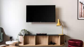 Una sala de estar moderna con un televisor montado, una mesa consola de madera, un reposapiés rojo y una lámpara de pie amarilla.