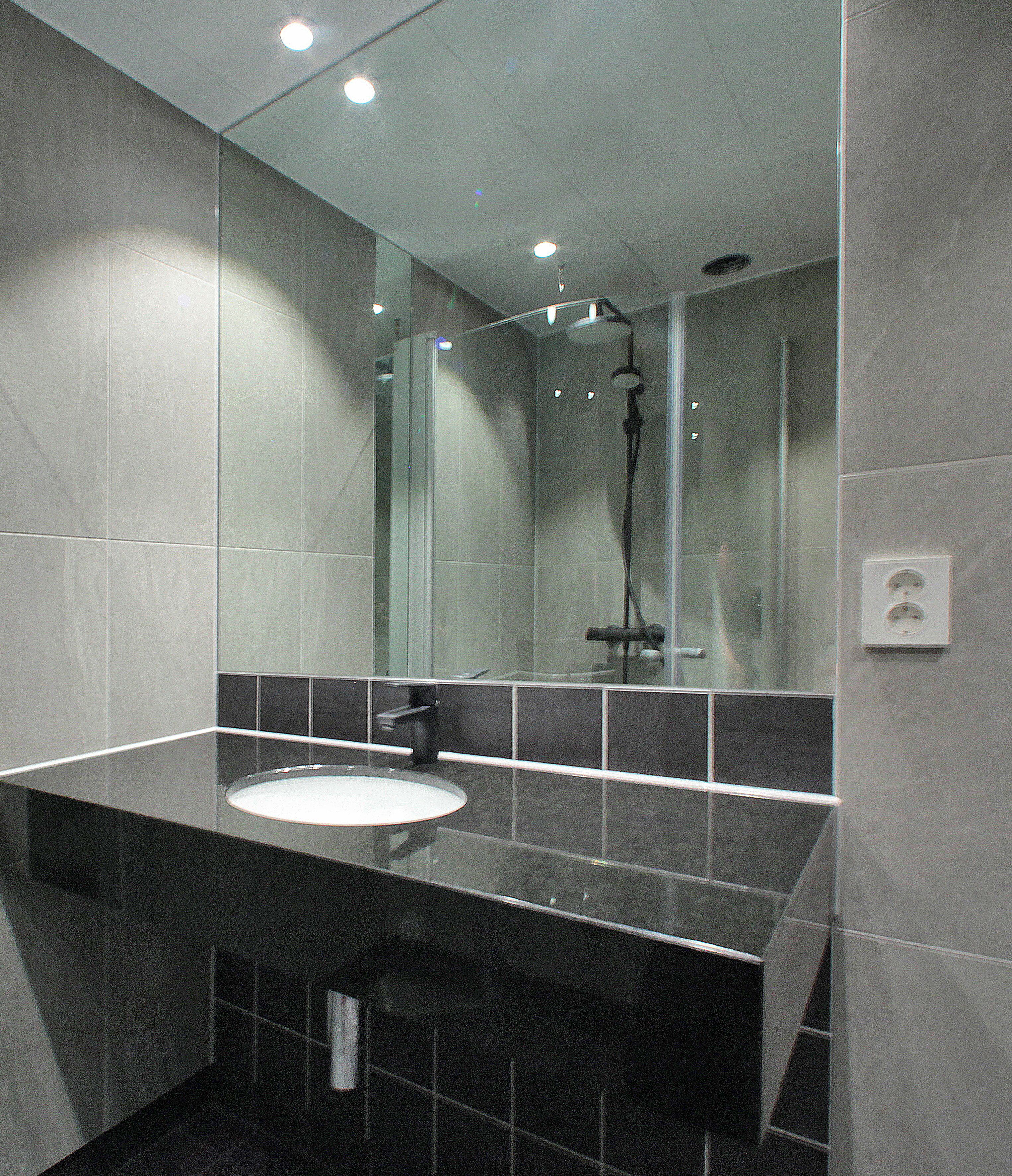 A modern bathroom with a black countertop, a white sink, and a glass shower enclosure.