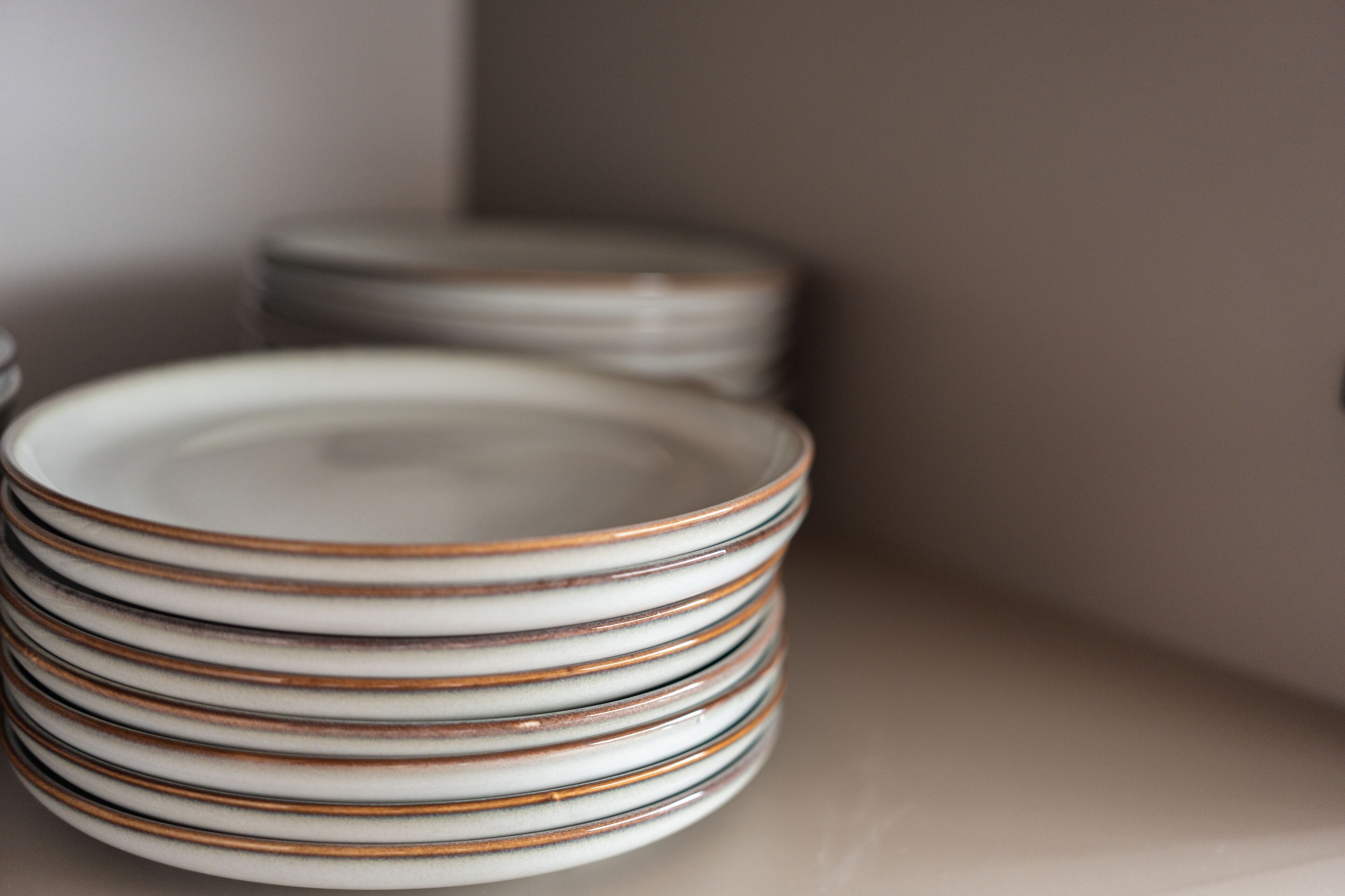 A stack of white plates with brown stripes on a beige surface.