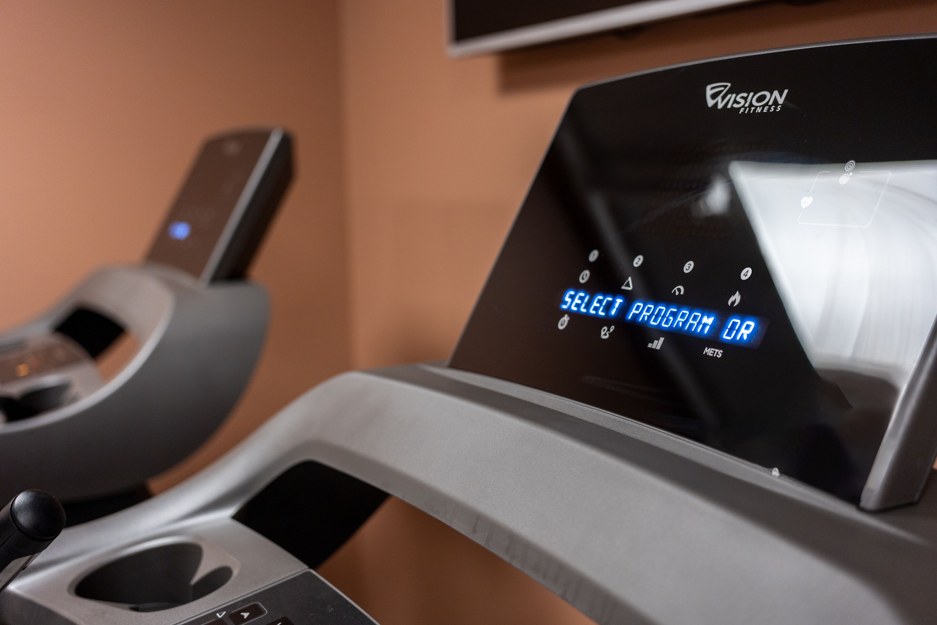 A treadmill with a digital display instructing to "SELECT PROGRAM OR METS."