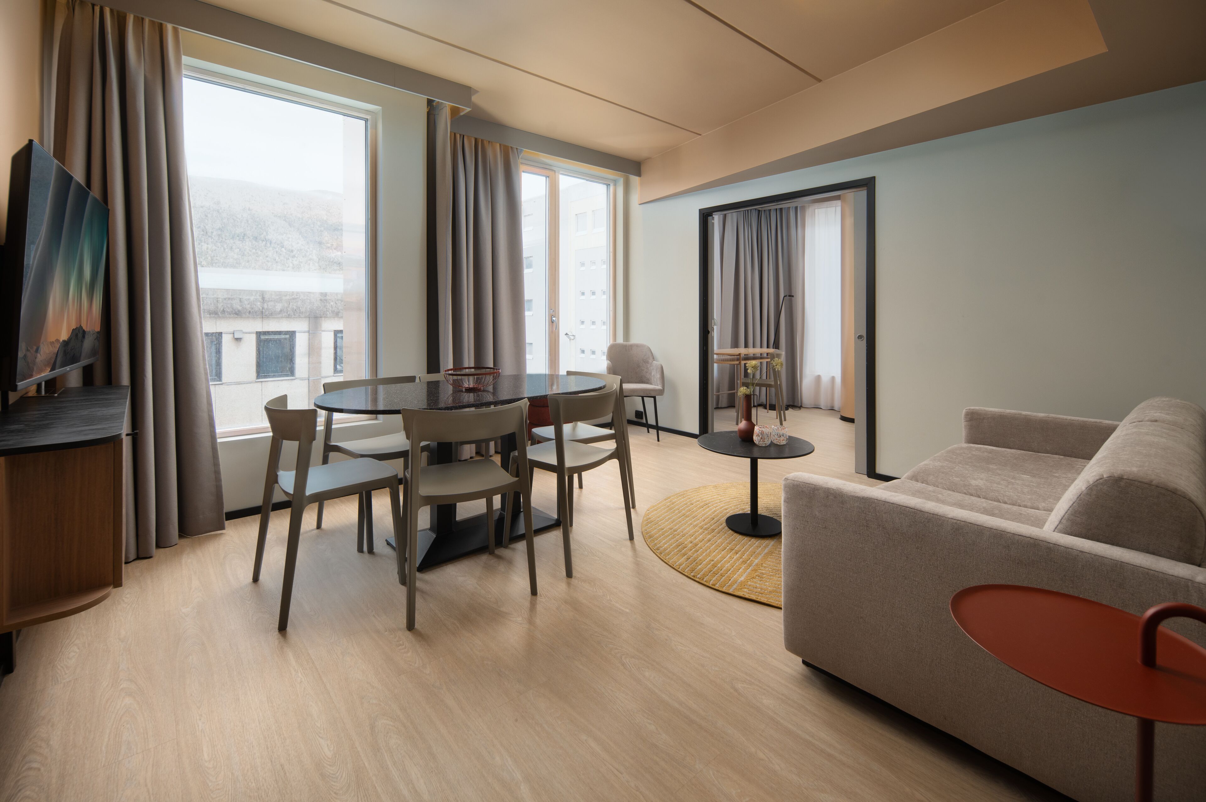 Una habitación de hotel moderna con zona de comedor, sofá y televisor.