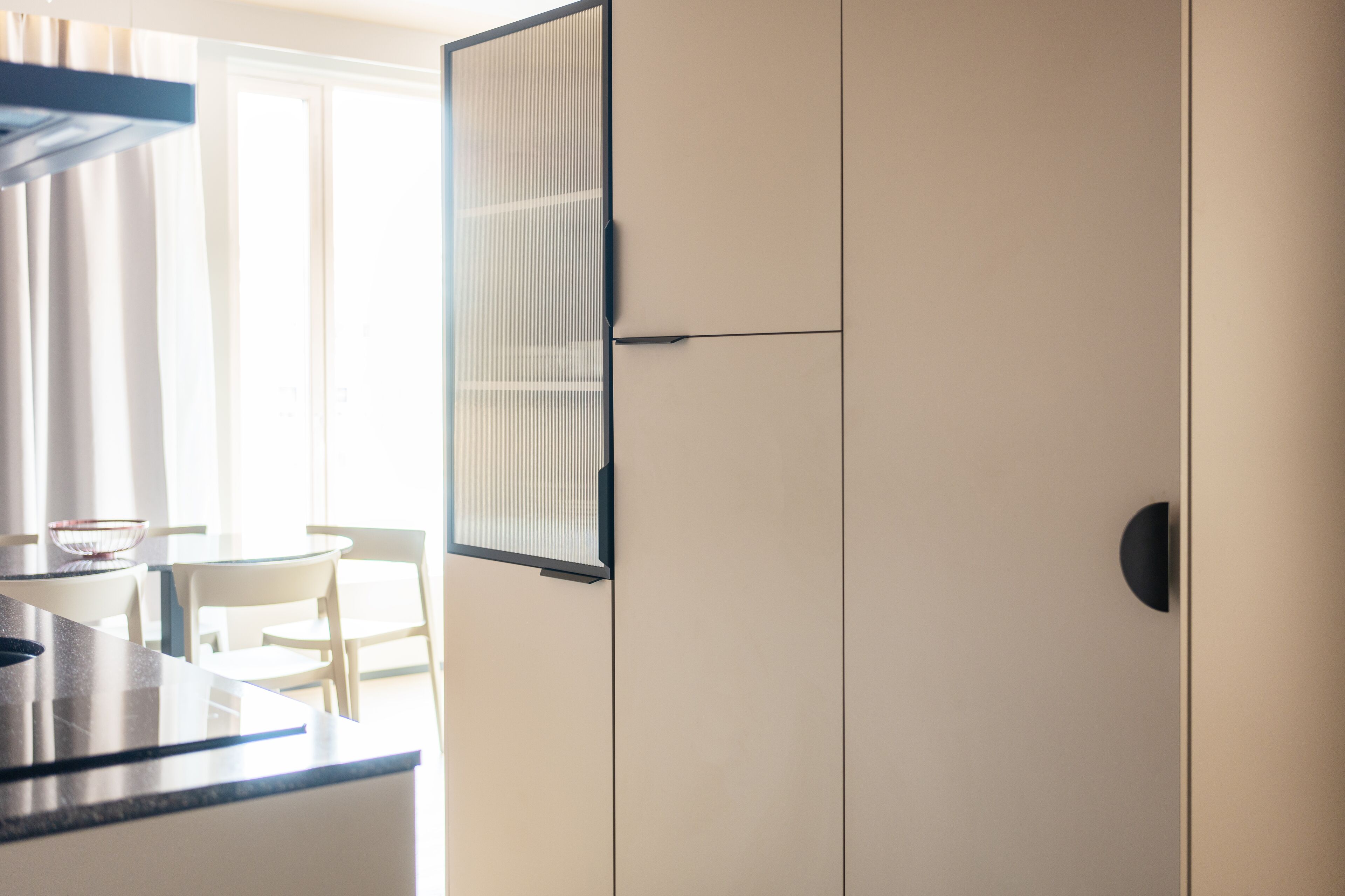 A modern kitchen with a built-in stove, a dining area with a table and chairs, and a large window allowing natural light.