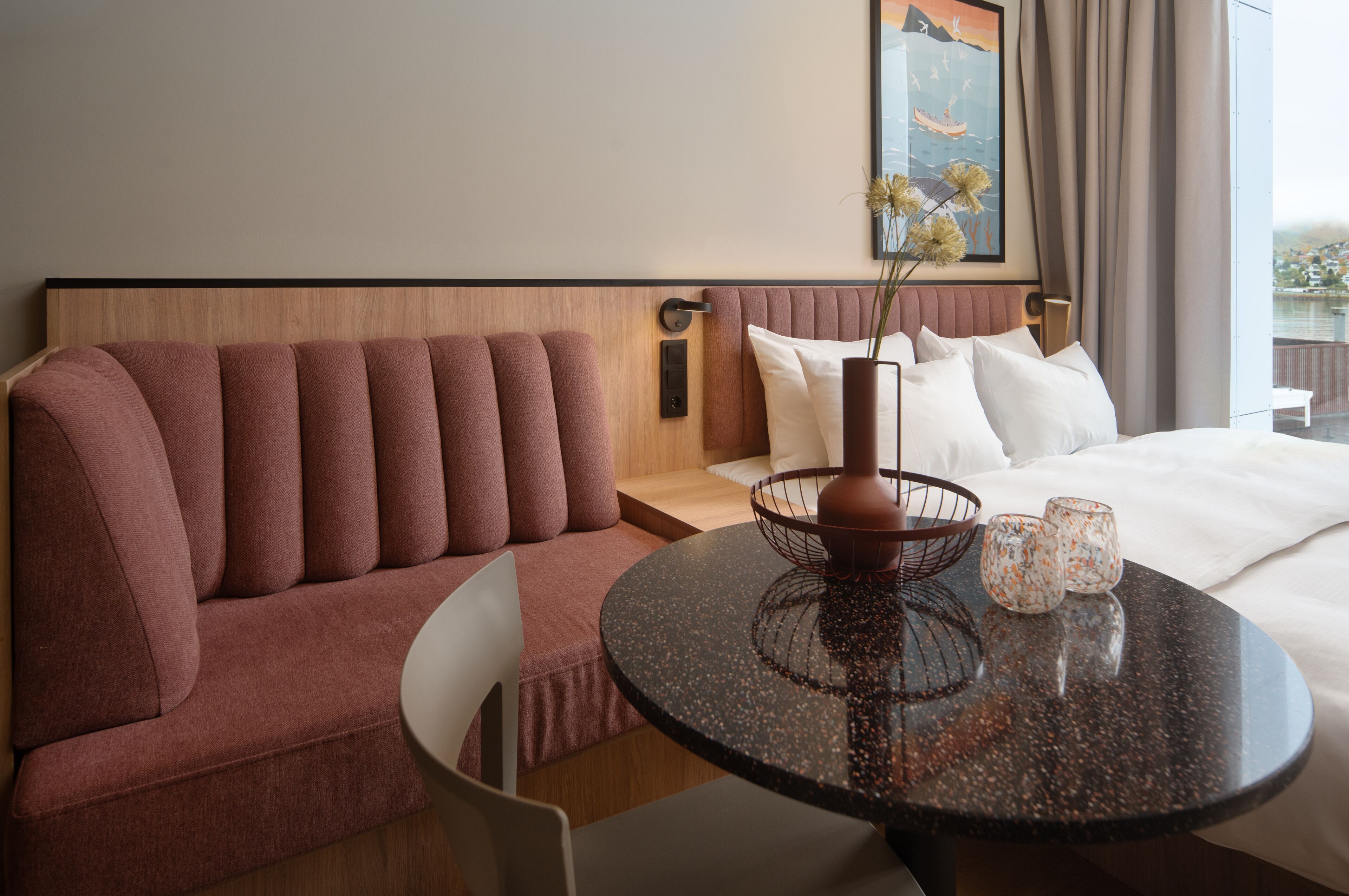 Habitación de hotel con una cama grande, una mesa redonda con un florero y vasos, un sofá y un cuadro en la pared.