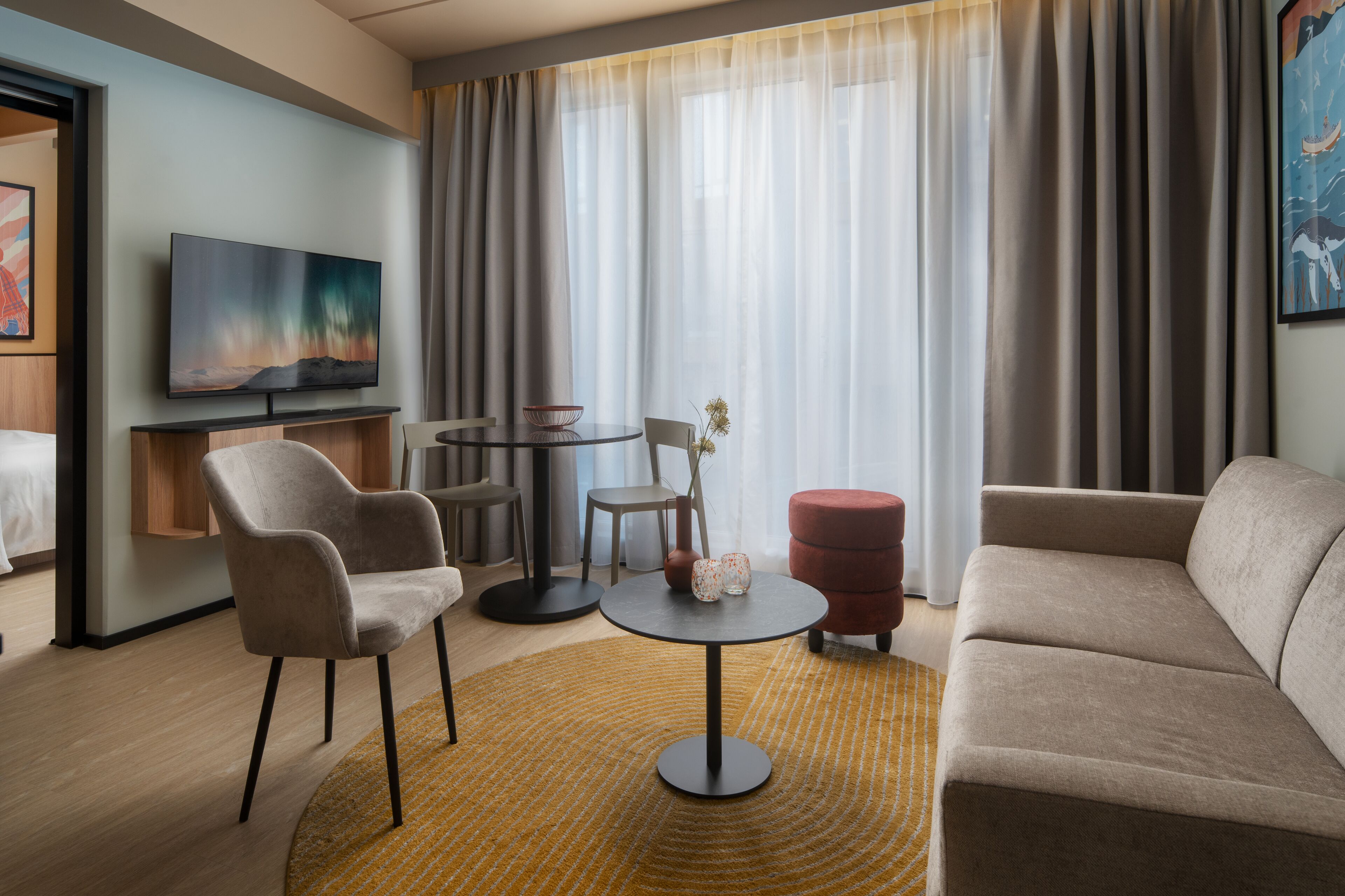 Habitación de hotel con sofá, sillón, mesa redonda y televisor en la pared.