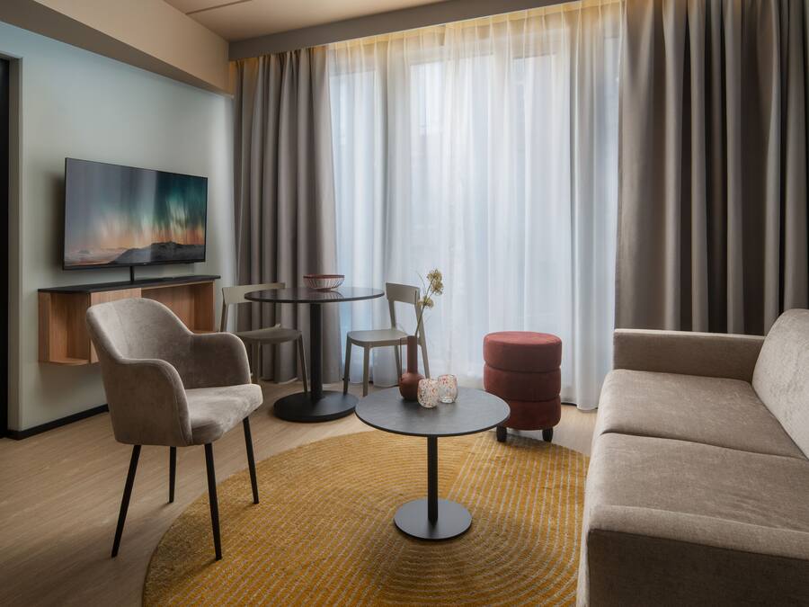 Habitación de hotel con sofá, sillón, mesa redonda y televisor en la pared.