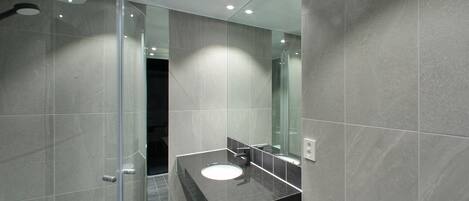A modern bathroom with a glass shower enclosure, a sink with a mirror, and tiled walls.