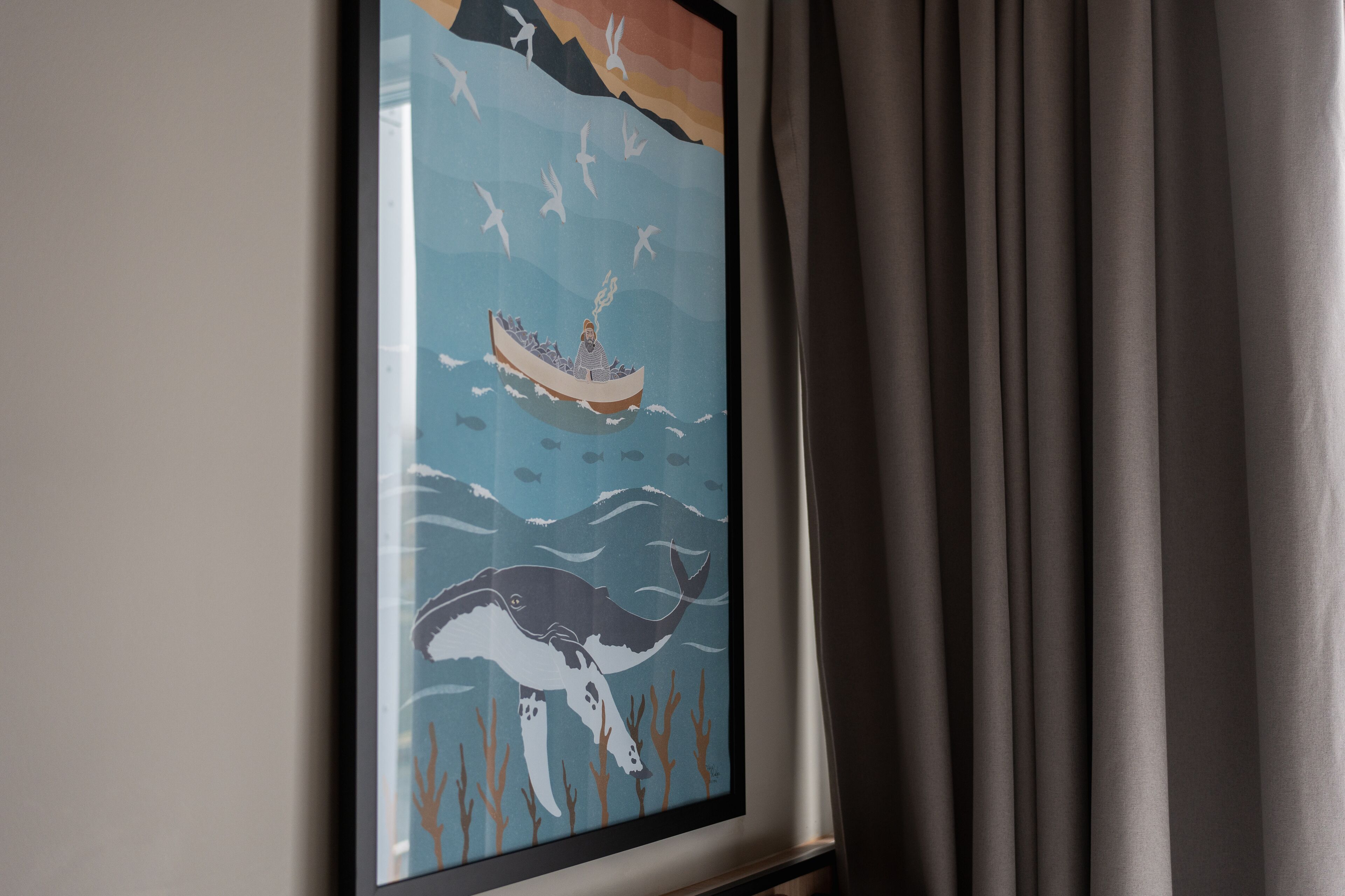 Een ingelijste afbeelding van een boot met een persoon en een walvis, voor een muur.