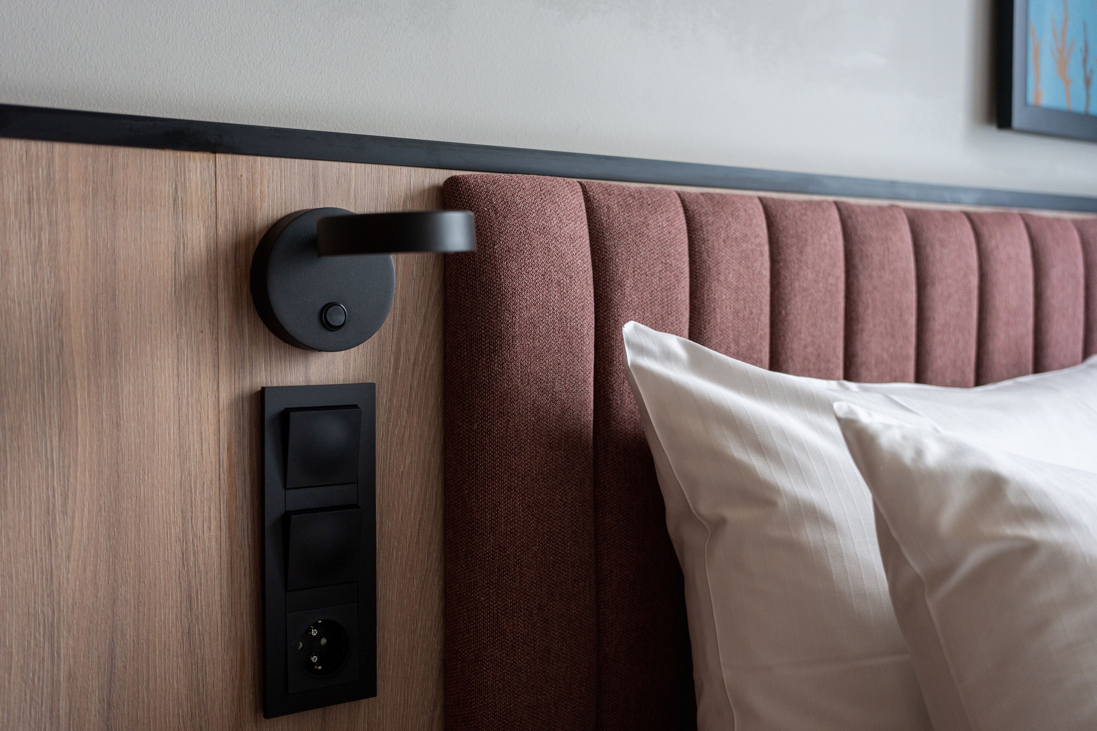 A modern hotel room with a wooden headboard, a black wall control panel, and a white pillow.
