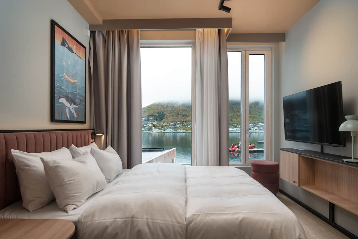 A hotel room with a large bed, a TV, and a view of a lake and mountains.