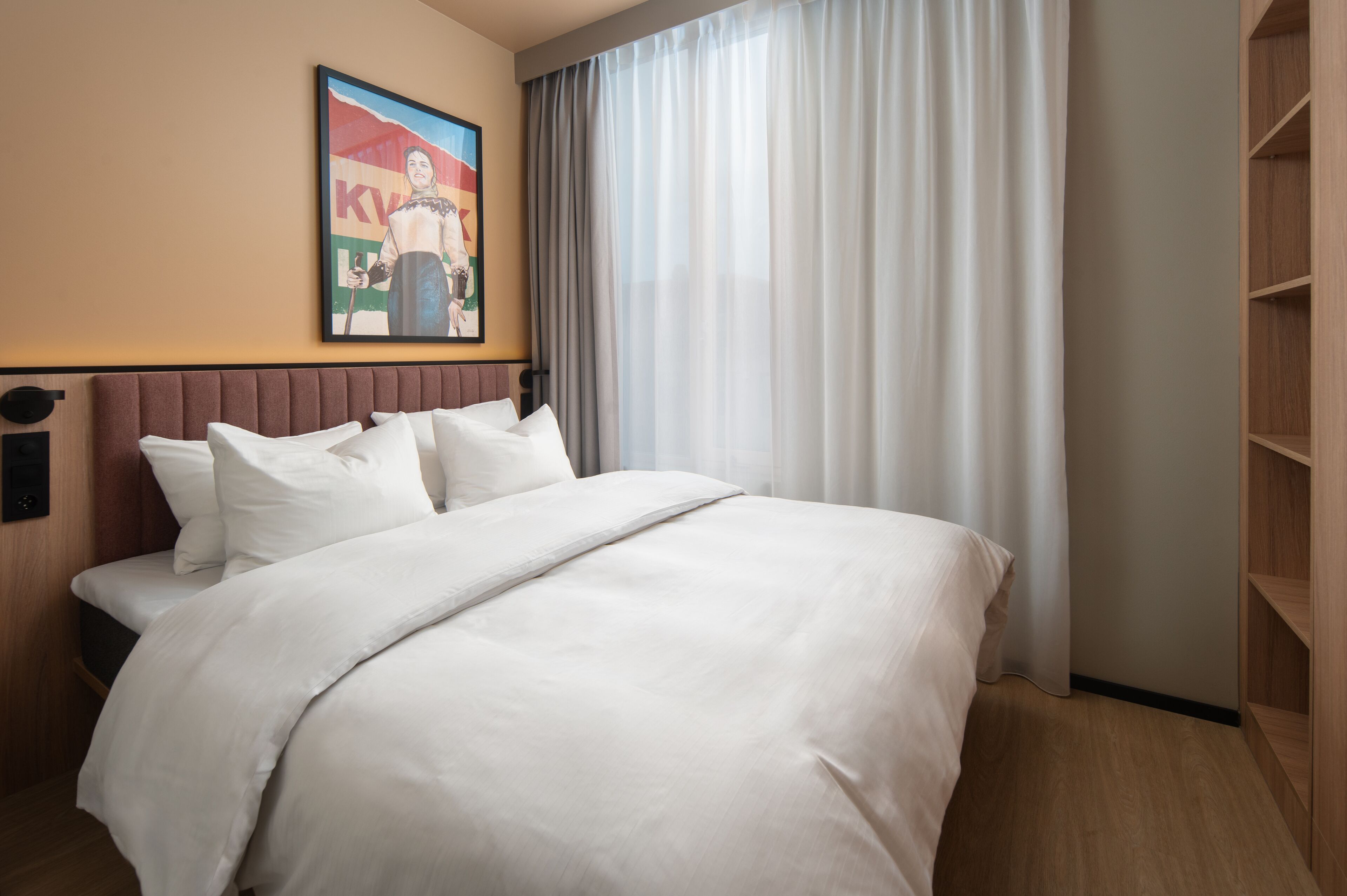 Habitación de hotel con una cama grande, cabecera, un cuadro en la pared y una ventana con cortinas.