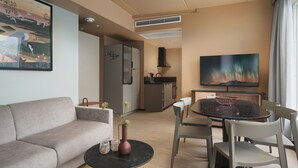 A modern hotel room with a sofa, a round dining table with chairs, a small kitchen area, and a flat-screen TV mounted on the wall. - Skaret by Vander (Tromsø)