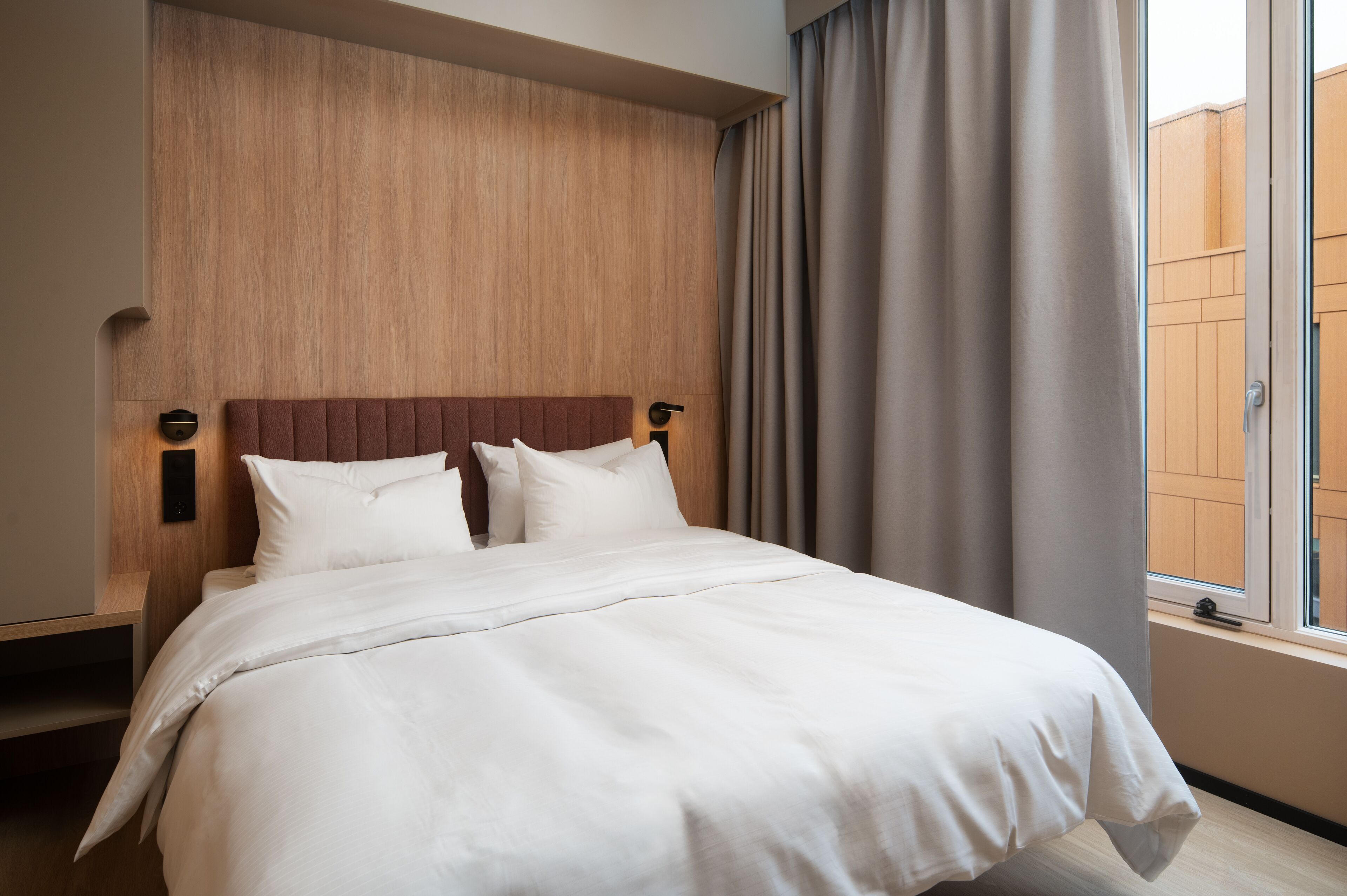 Un lit bien fait, avec du linge de lit blanc, une tête de lit en bois et une fenêtre avec des rideaux.