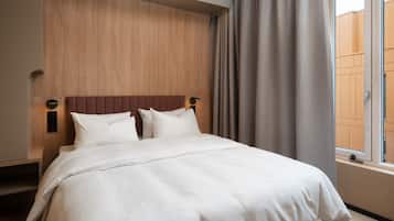Un lit bien fait, avec du linge de lit blanc, une tête de lit en bois et une fenêtre avec des rideaux.
