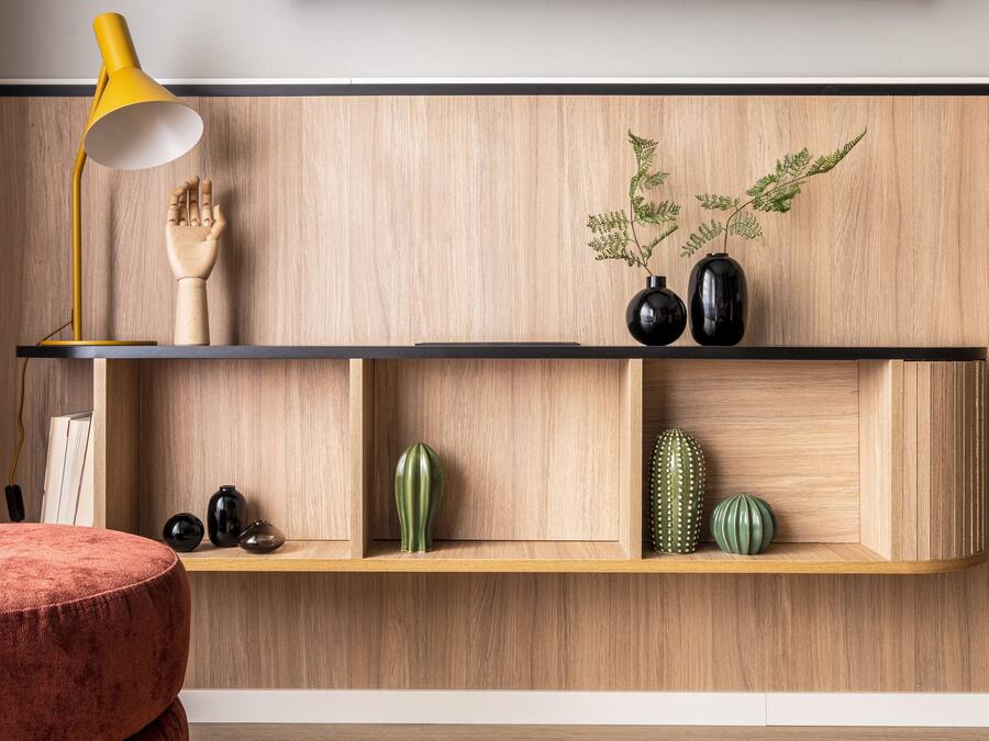 A modern interior with wooden shelves displaying decorative items, a yellow desk lamp, and a red ottoman.