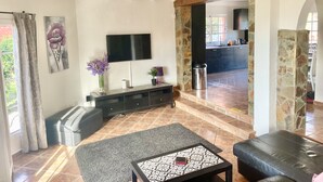 A modern living room with a stone column, a flat-screen TV, a sofa, a coffee table, and a view into the kitchen. - Spacious Villa in Quiet Location Close to Resorts (Buzanada)