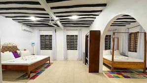 A hotel room with two beds, a ceiling fan, and a large window with shutters. - Five Palms Bwejuu (Bwejuu)