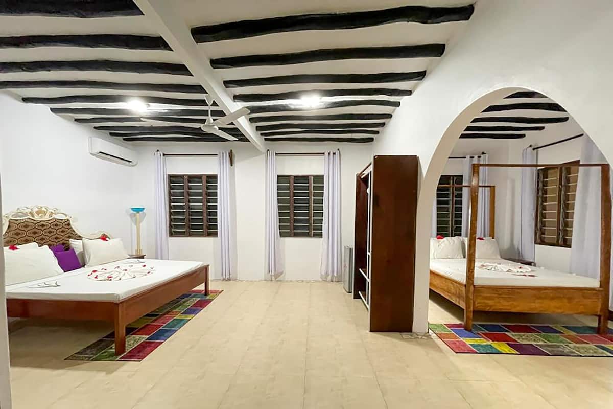 Habitación de hotel con dos camas, un ventilador de techo y un ventanal con contraventanas.