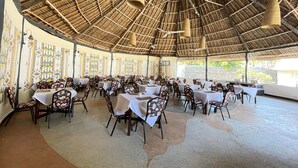 A spacious indoor dining area with high ceilings and thatched roof. Tables are set with white tablecloths and floral chairs. - Five Palms Bwejuu (Bwejuu)