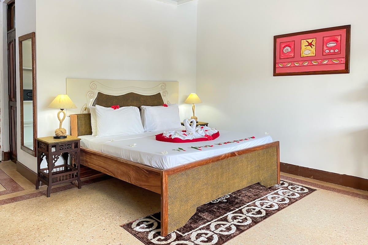 Habitación de hotel ordenada con cama, dos mesitas de noche, un espejo y un adorno en la pared.