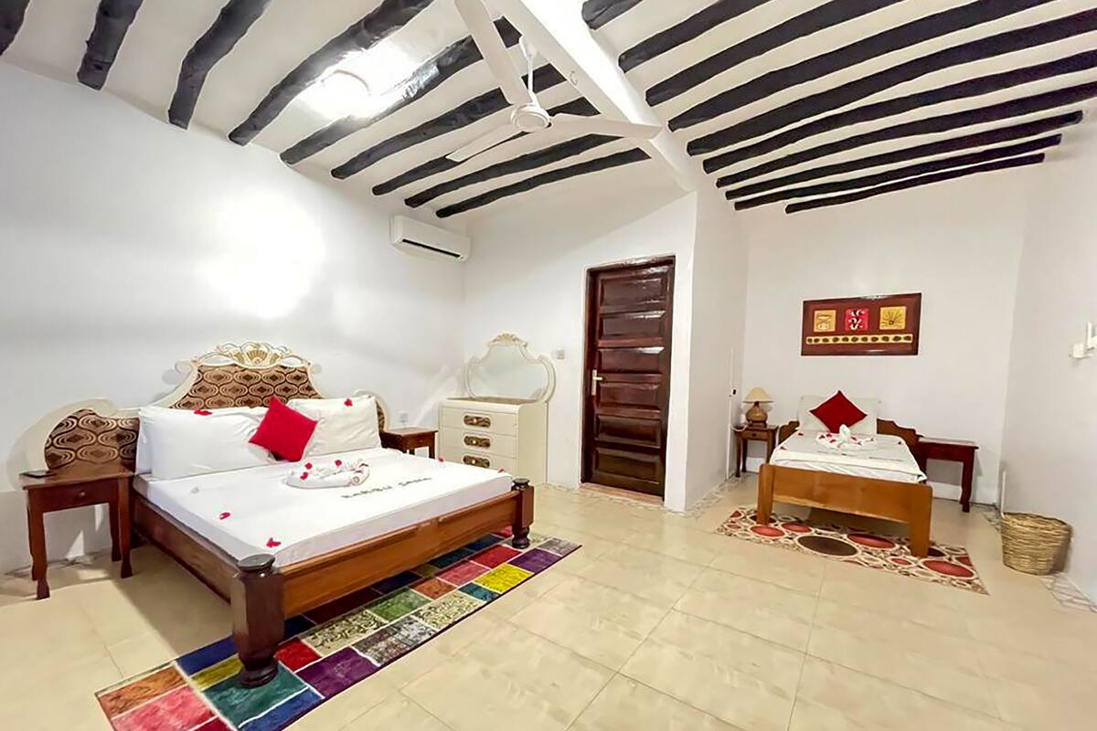 Un dormitorio con cama, cómoda, mesita de noche, espejo, puerta y una pequeña mesa con lámpara.
