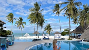 A poolside area with a clear view of the ocean, palm trees, and a thatched-roof structure. - Five Palms Bwejuu (Bwejuu)