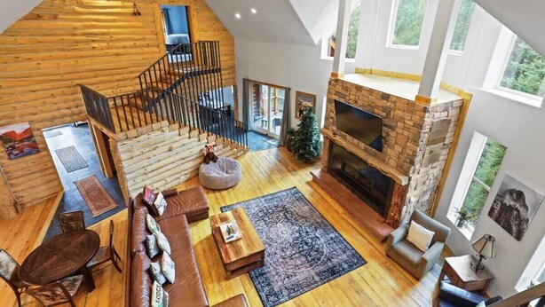 A spacious loft-style living area with a stone fireplace, wooden floors, and a staircase leading to an upper level. - Spacious 7BR Lodge with Mountain Views! (Breckenridge)