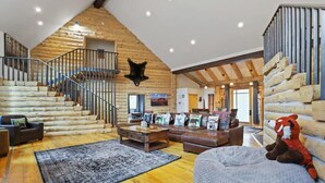 A log cabin interior with a staircase, wooden walls, a fireplace, a sofa, a coffee table, and a stuffed animal. - Spacious 7BR Lodge with Mountain Views! (Breckenridge)