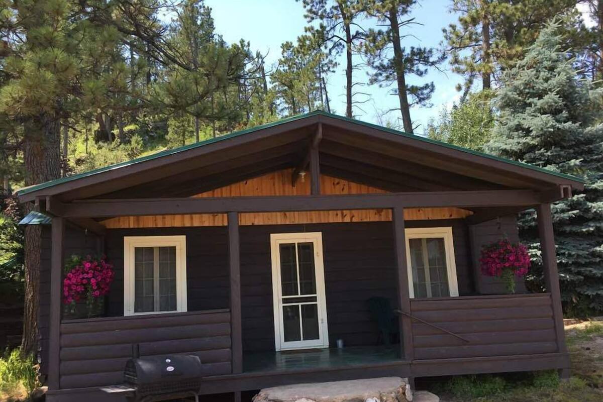 A cabin with a porch, a grill, and a stone fire pit.