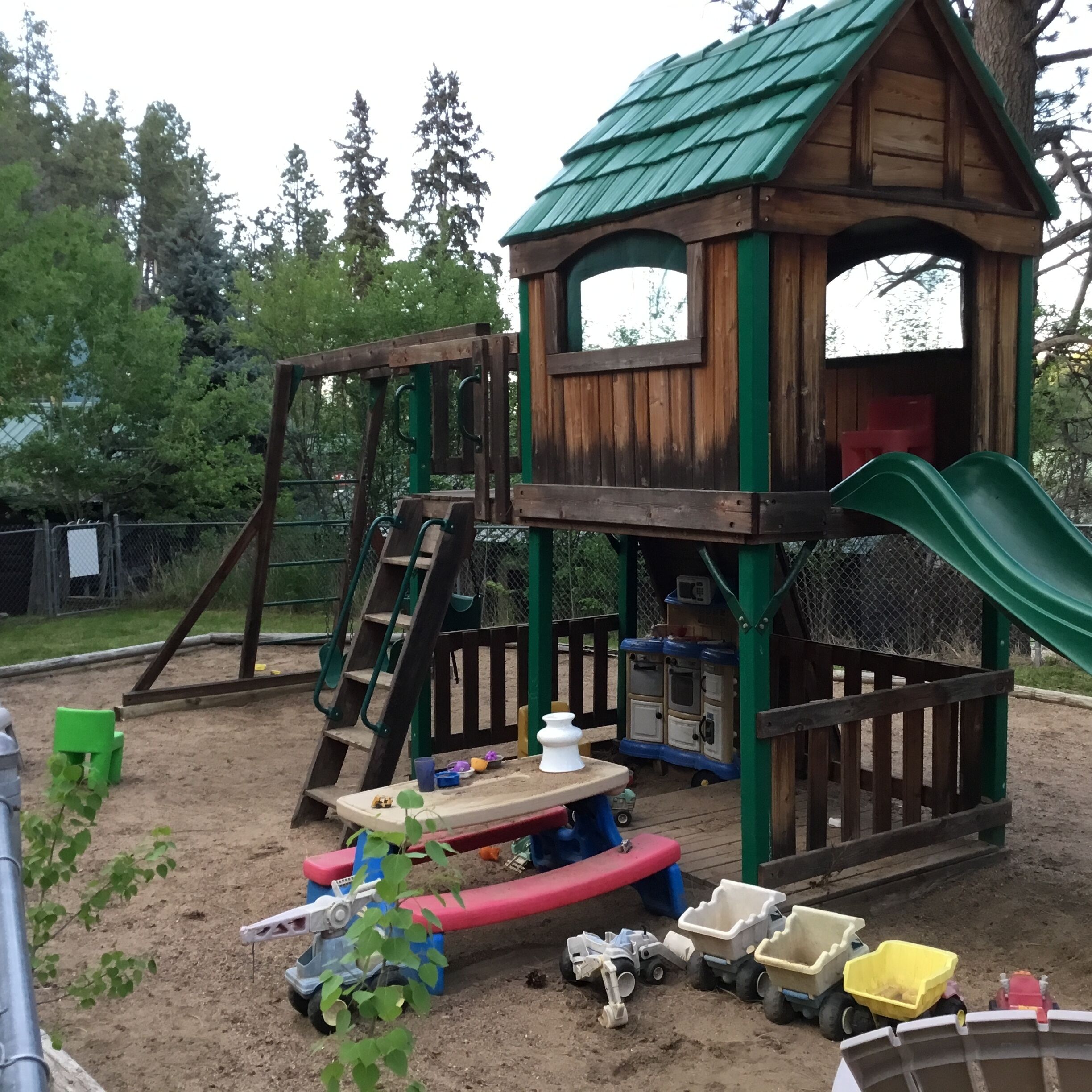A children's play area with a wooden playhouse, a slide, and various play equipment.