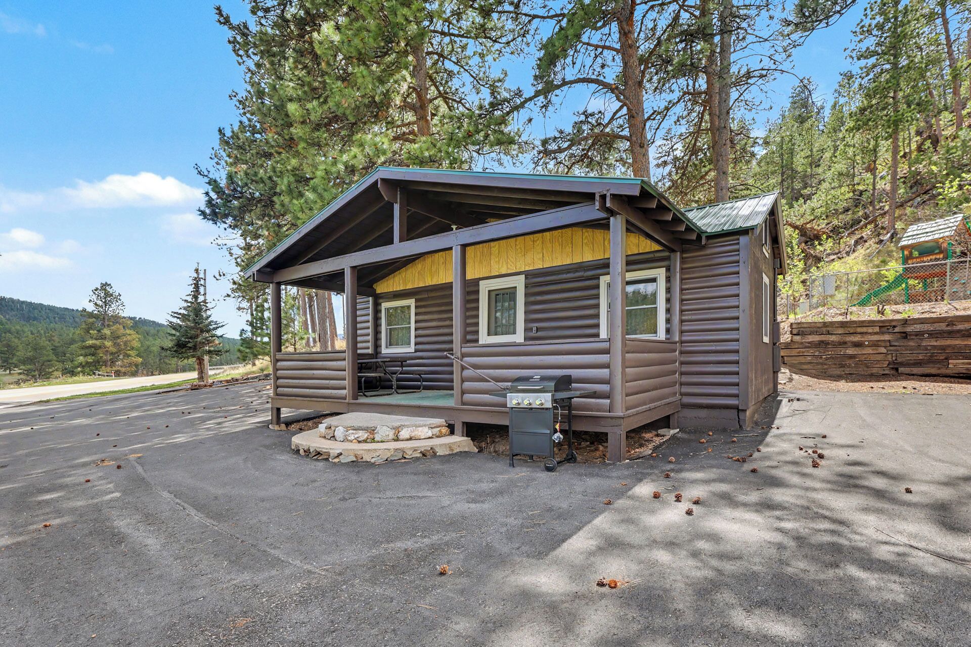 Une petite cabane avec une véranda, un barbecue et un banc en pierre.