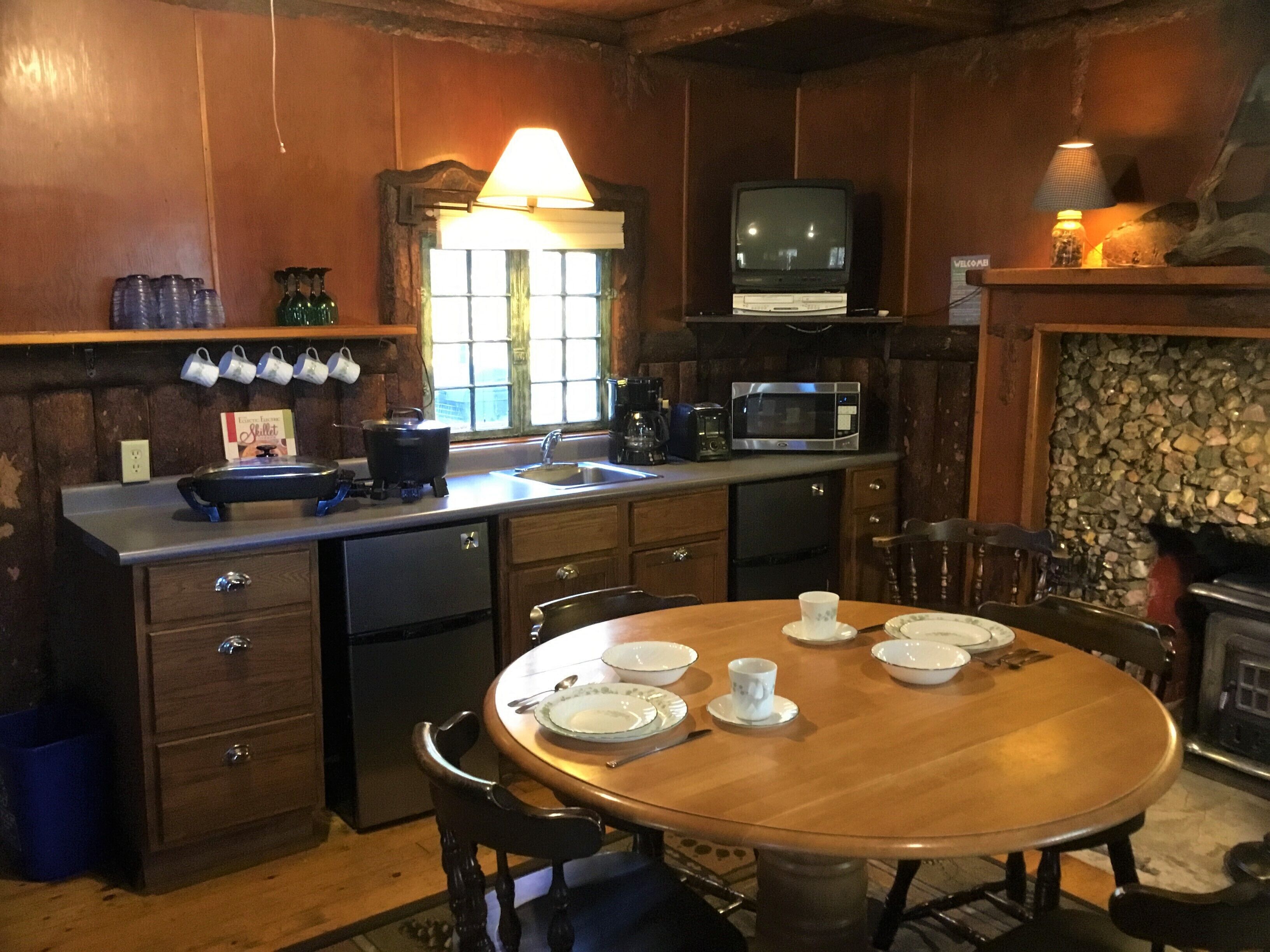 Uma cozinha acolhedora com armários de madeira, uma mesa de jantar posta para quatro pessoas e uma lareira de pedra.