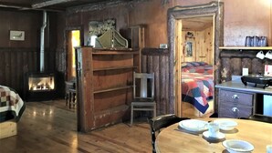 A cozy room with a wooden interior, a bed with a colorful quilt, a small table with plates and cups, and a chair. - Timber Haven Cabins (Hill City)