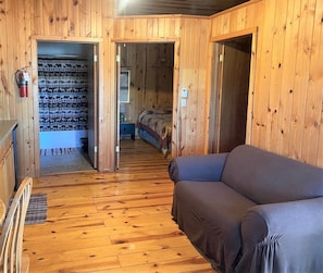 A wooden cabin interior with a sofa, a bed, and a bathroom visible through an open door.