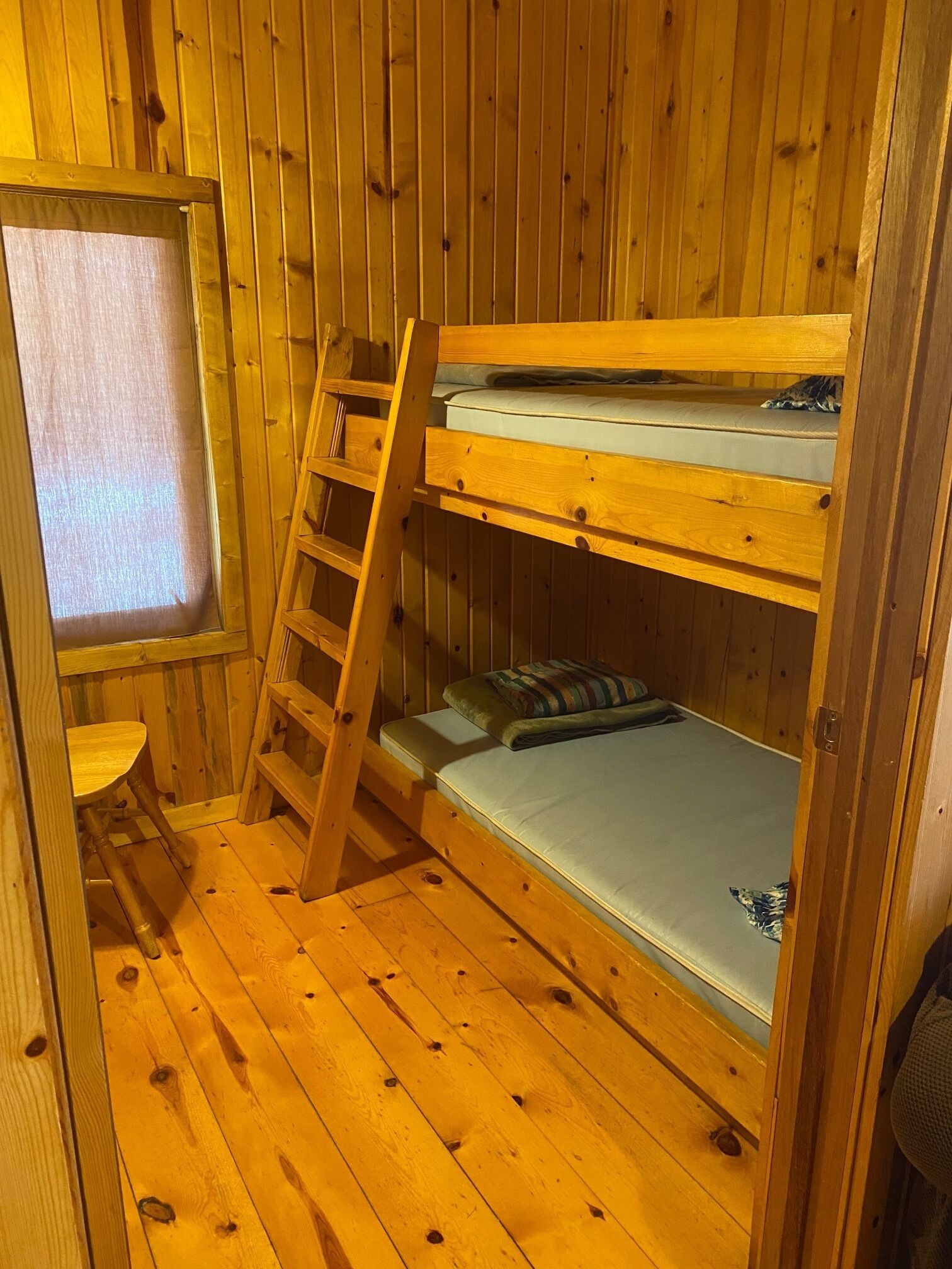 Habitación con literas de madera, una escalera, una mesita y una ventana.