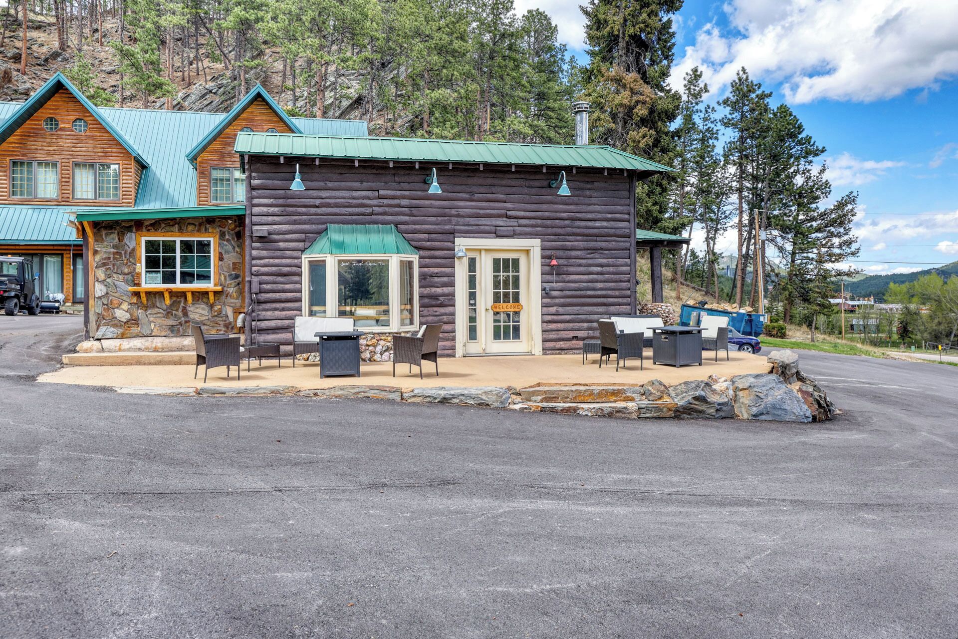 A log cabin with a stone foundation, a green roof, and a patio with outdoor furniture.