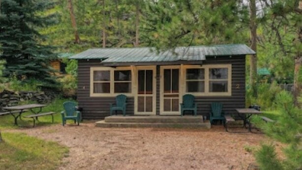 A small cabin with a porch, two green chairs, and a picnic table. - Timber Haven Cabins (Hill City)