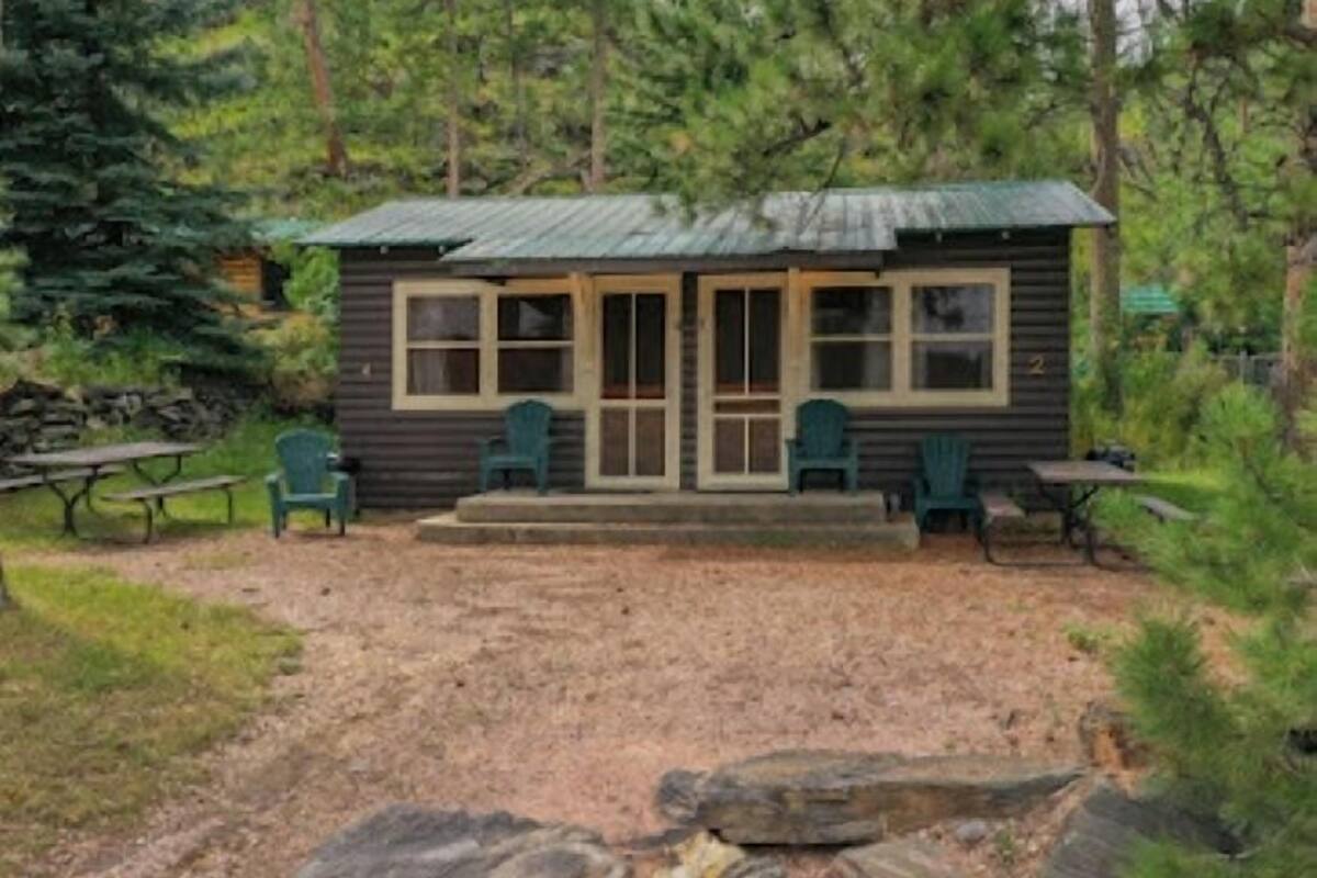 A small cabin with a porch, two green chairs, and a picnic table.