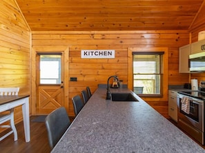 Enjoy meal preparation in this cozy cabin kitchen with a long countertop, sink, and stove.